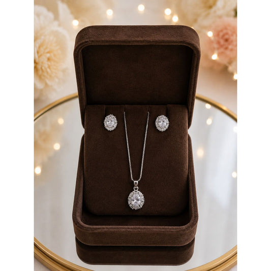 Oval crystal pendant necklace and matching stud earrings displayed in a premium chocolate brown velvet jewelry box with soft ambient lighting.