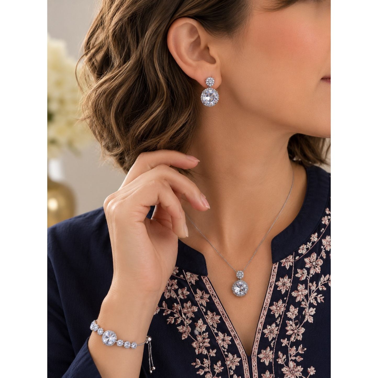 Model wearing a silver crystal jewelry set featuring round crystal drop earrings, matching pendant necklace, and adjustable crystal bracelet with a navy embroidered outfit.