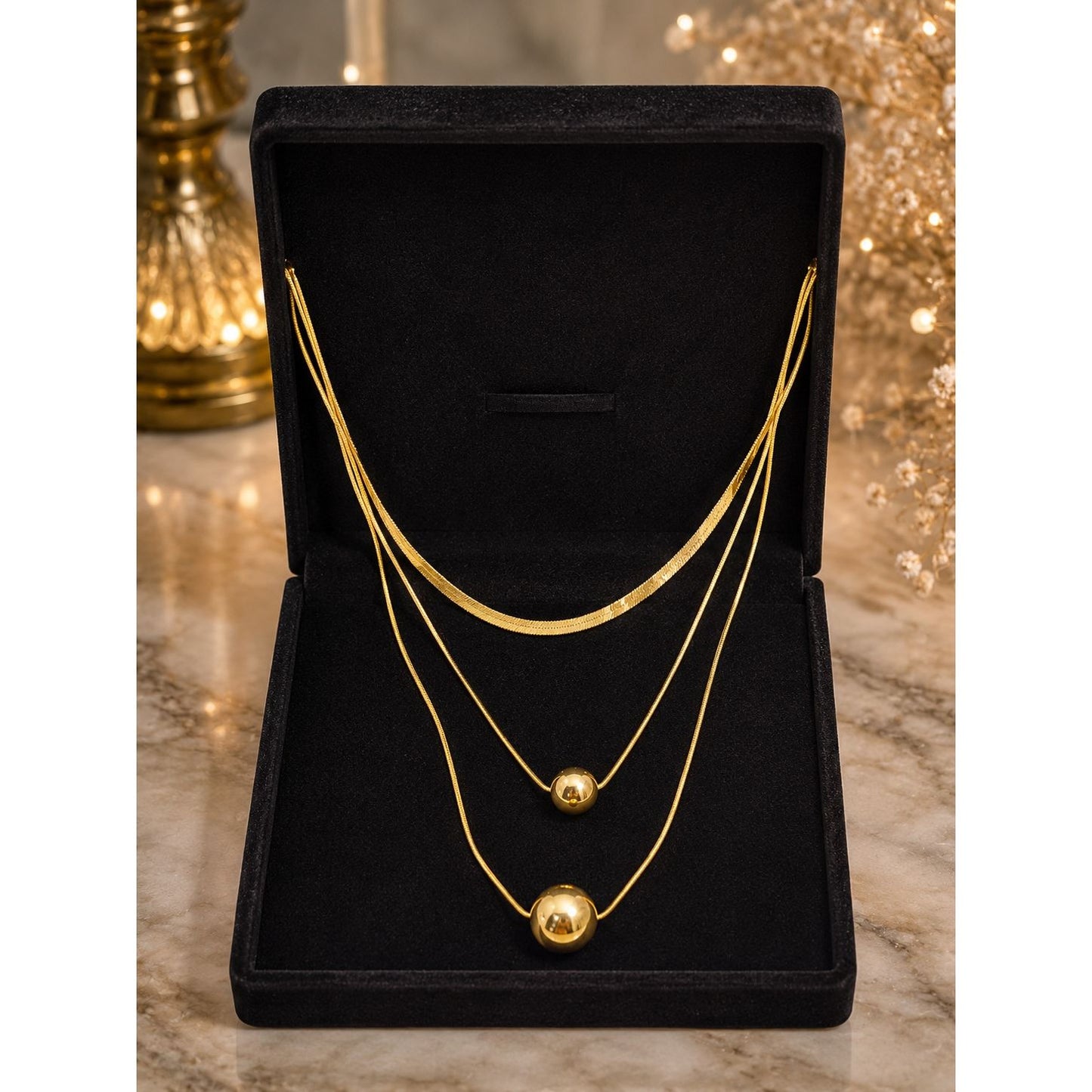 Layered gold necklace with polished sphere pendants displayed in a premium black velvet jewelry box on a marble surface.
