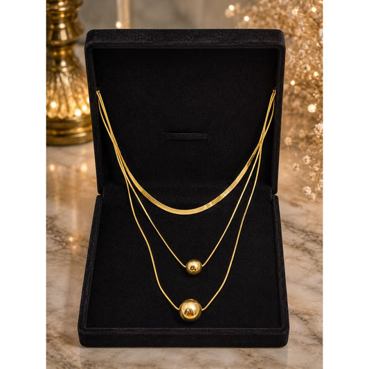 Layered gold necklace with polished sphere pendants displayed in a premium black velvet jewelry box on a marble surface.