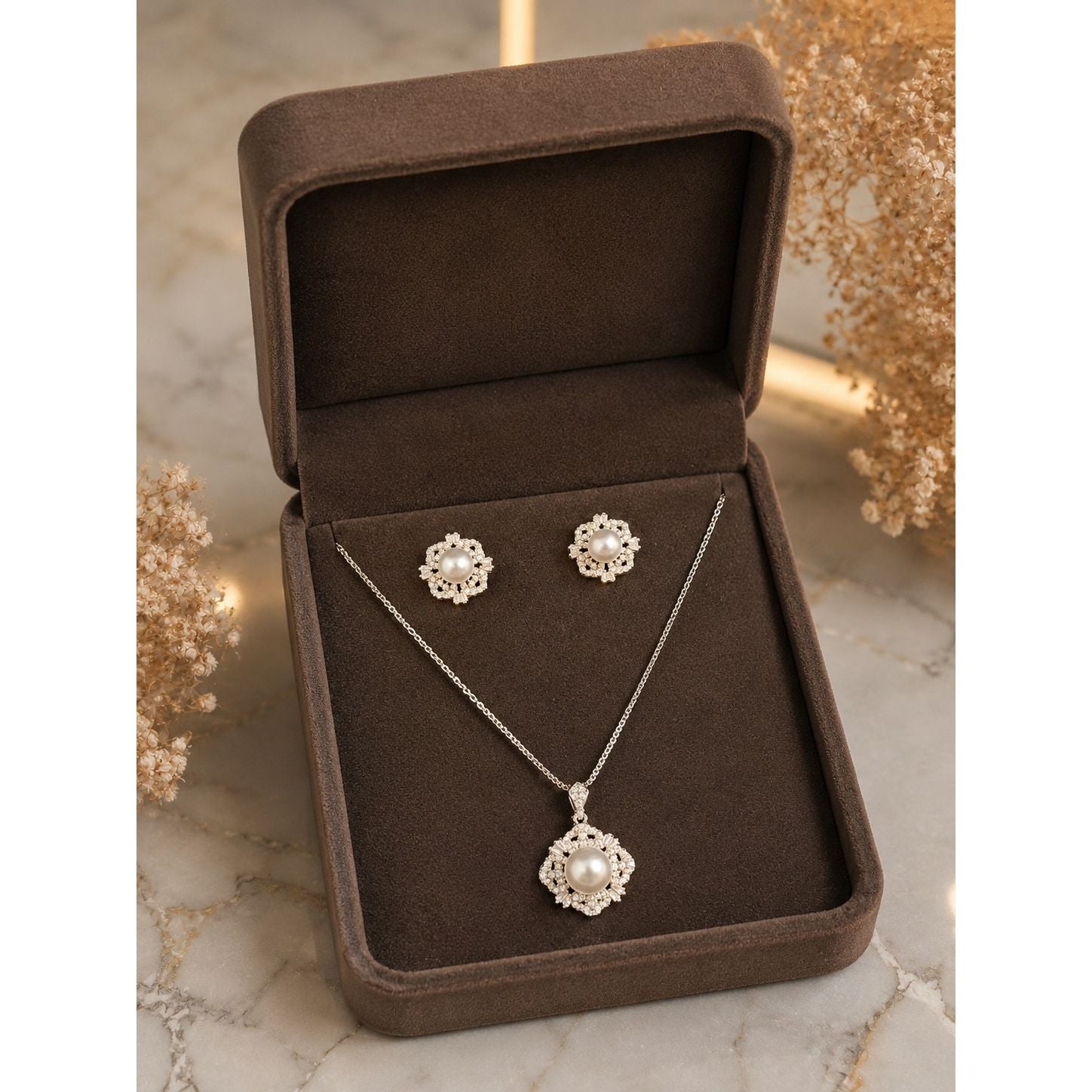Pearl and crystal floral necklace and stud earrings set displayed in a premium brown velvet jewelry box on a marble surface.