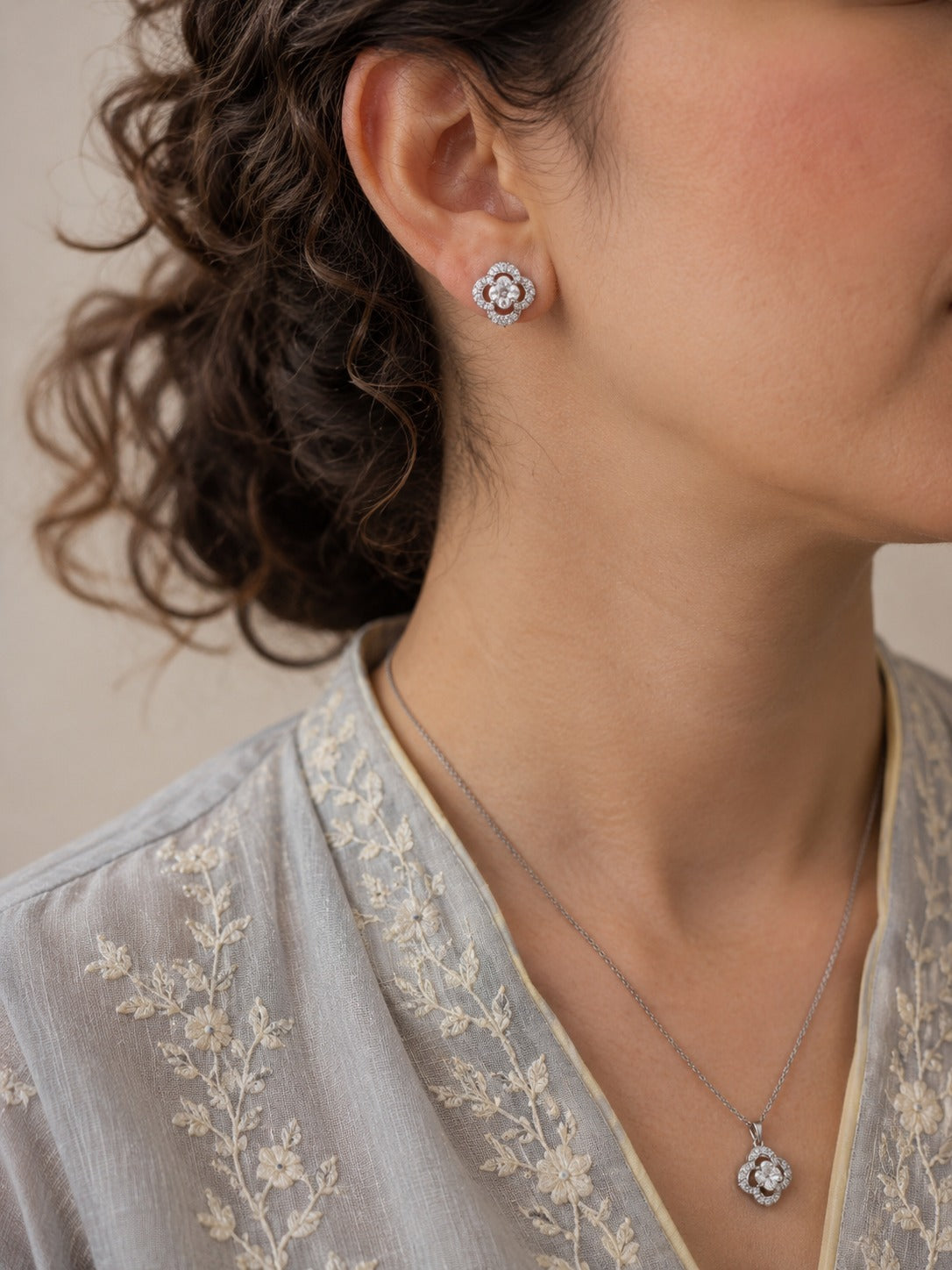 Woman wearing a crystal clover necklace and matching stud earrings styled with a soft embroidered outfit, showcasing a floral-inspired silver-tone jewelry set.