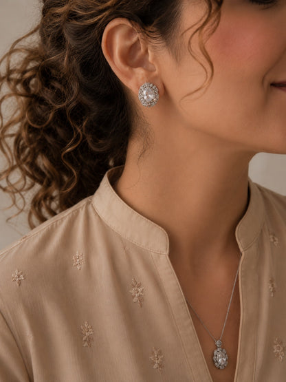 Woman wearing a silver-tone crystal halo necklace and matching oval crystal stud earrings with a soft beige embroidered outfit, showcasing a timeless formal jewelry set.