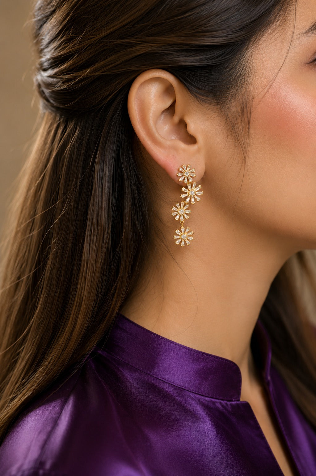 Gold floral cubic zirconia drop earrings worn by model with plum satin shirt, showcasing four cascading flower motifs.