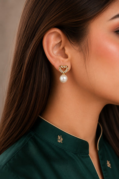 Gold heart-shaped cubic zirconia pearl stud earrings worn by model with emerald green satin shirt, featuring a classic pearl drop.
