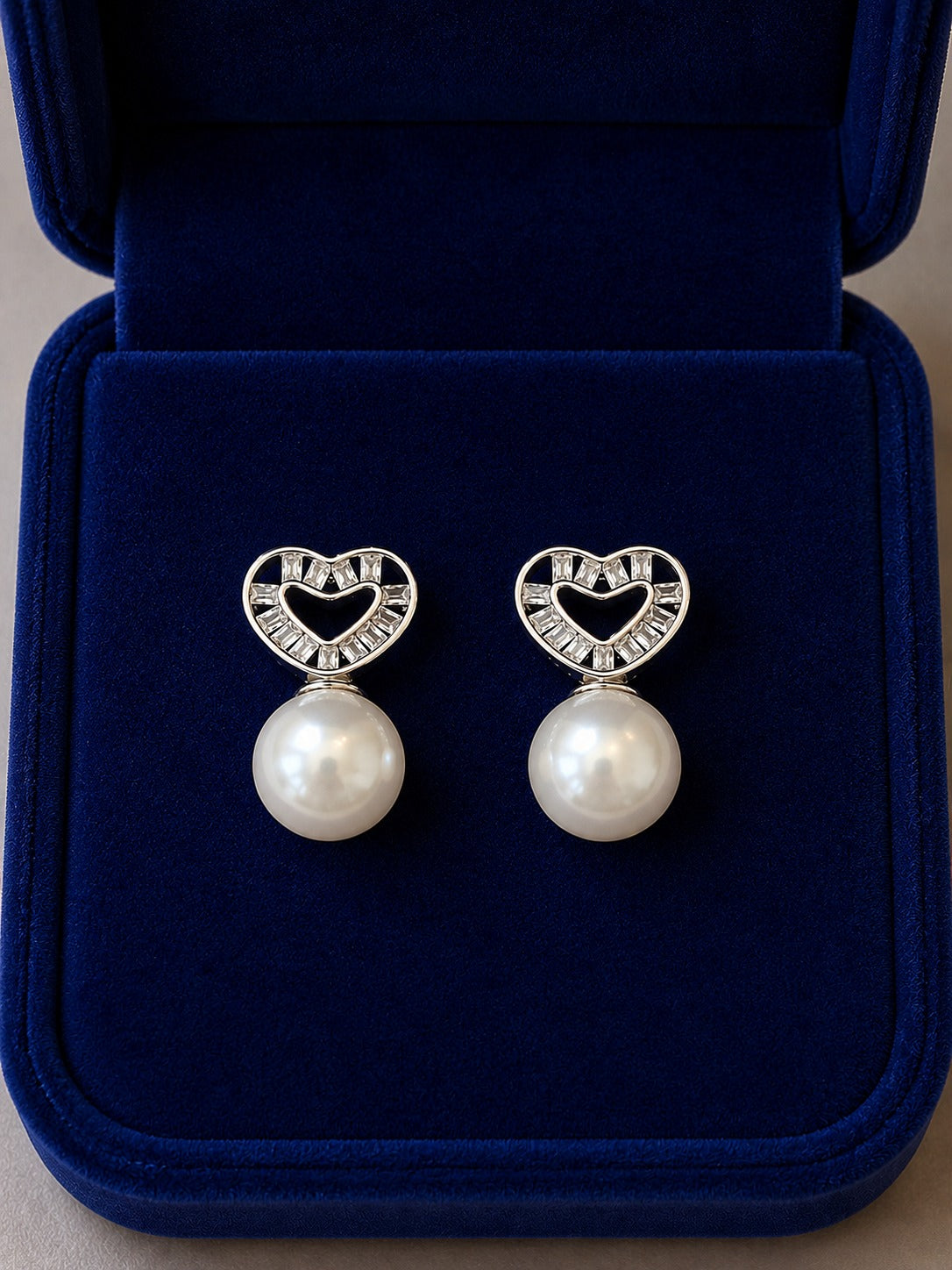 Silver heart pearl stud earrings with cubic zirconia displayed inside a premium navy velvet jewellery box.
