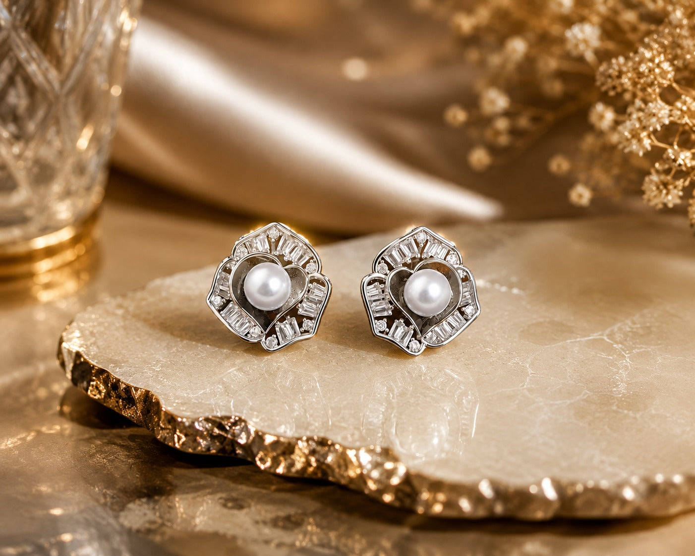 Silver-tone pearl and crystal floral stud earrings displayed on a premium natural stone slab with a luxury decorative background and warm ambient lighting.