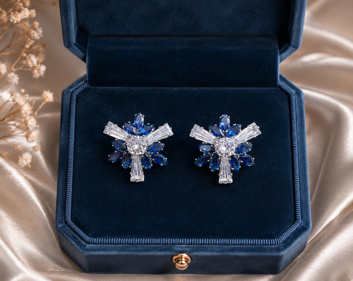Sapphire blue floral crystal stud earrings displayed in a premium navy velvet jewelry box with warm luxury décor.