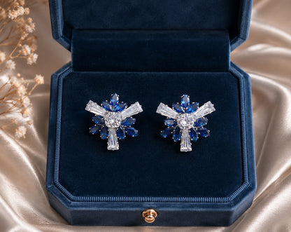 Sapphire blue floral crystal stud earrings displayed in a premium navy velvet jewelry box with warm luxury décor.