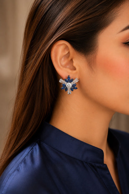 Model wearing sparkling lblue crystal floral stud earrings in a silver-tone finish with a navy satin shirt, highlighting premium statement earrings.