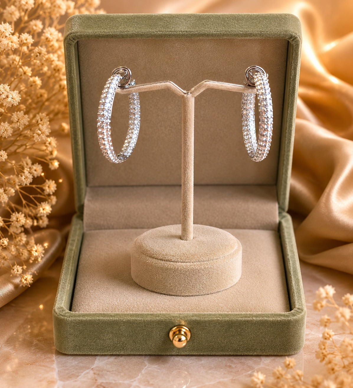 Silver crystal hoop earrings showcased on a premium velvet jewelry stand inside a sage green presentation box with soft luxury décor.