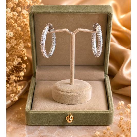Silver crystal hoop earrings showcased on a premium velvet jewelry stand inside a sage green presentation box with soft luxury décor.