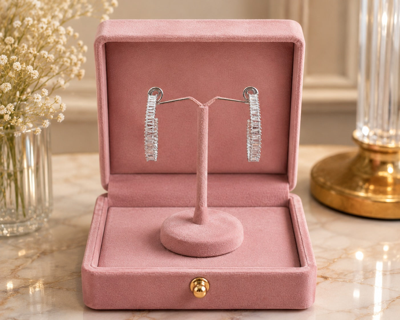 Silver-tone baguette crystal hoop earrings showcased on a premium velvet jewelry stand inside a blush pink jewelry box with a soft luxury interior setting
