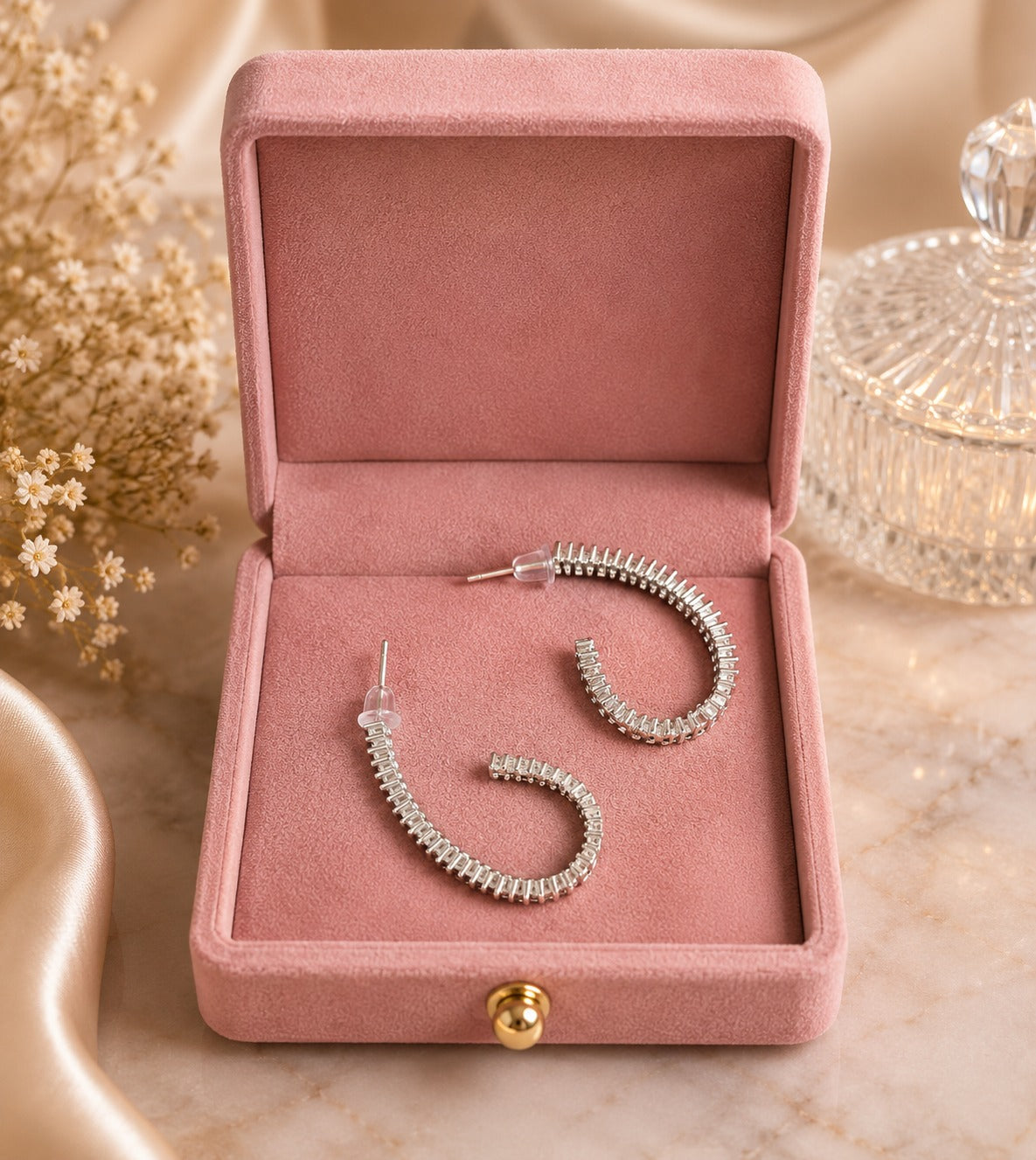 Silver-tone baguette crystal hoop earrings displayed inside a premium blush pink velvet jewelry box on a polished marble surface with luxury décor.