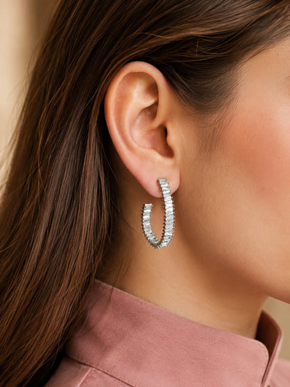 Model wearing silver-tone baguette crystal hoop earrings with a blush pink satin blouse, highlighting contemporary statement hoop earrings.