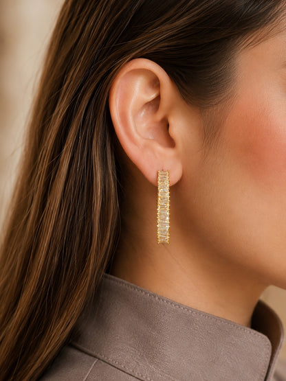 Model wearing gold-tone baguette crystal hoop earrings, styled with a taupe satin blouse, showcasing modern luxury hoop earrings.