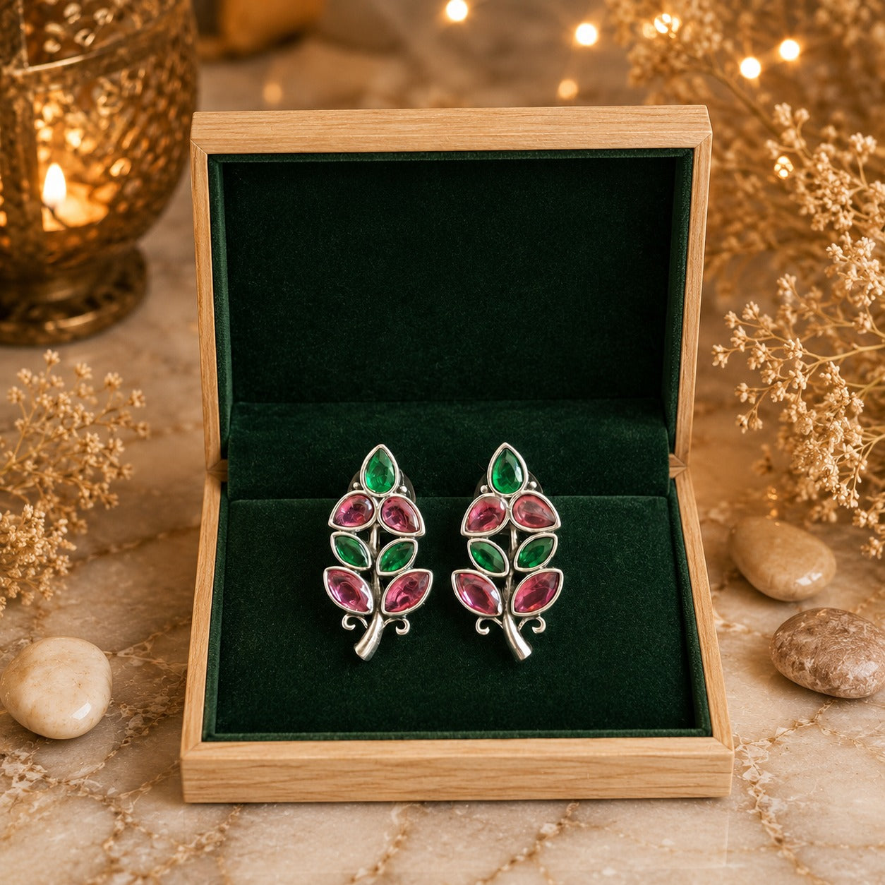 Pair of earrings with green and pink stones in a wooden box on a decorative surface.