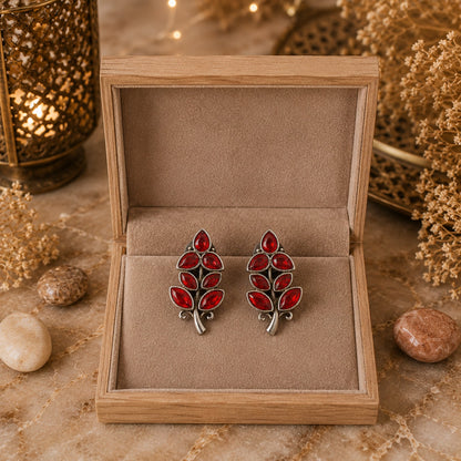 Red leaf-shaped earrings in a wooden box with a warm, earthy background.