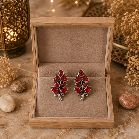 Red leaf-shaped earrings in a wooden box with a warm, earthy background.