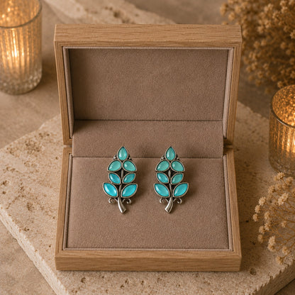 Pair of turquoise leaf-shaped earrings in a wooden jewelry box.