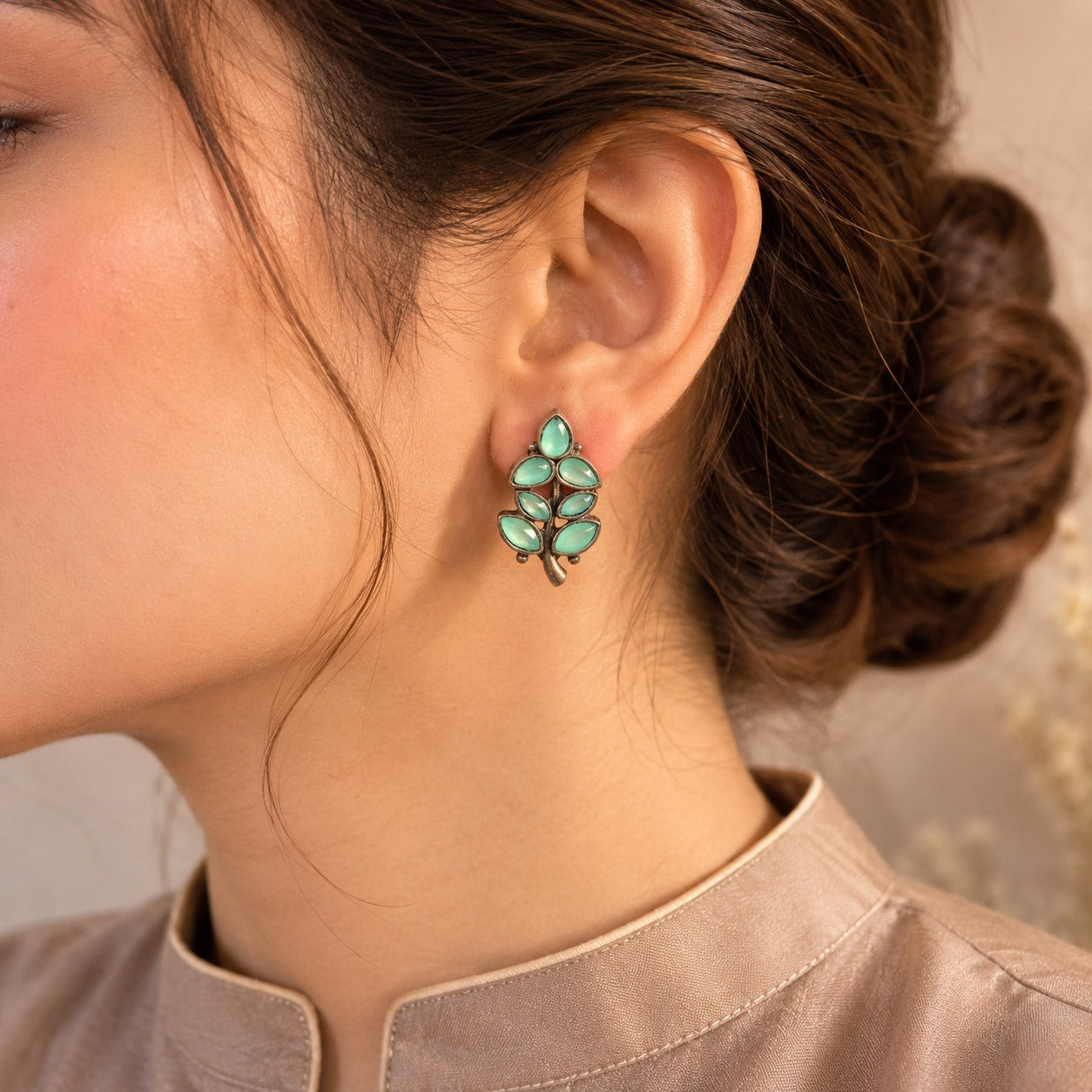 Close-up of a person wearing a green leaf-shaped earring with a neutral background