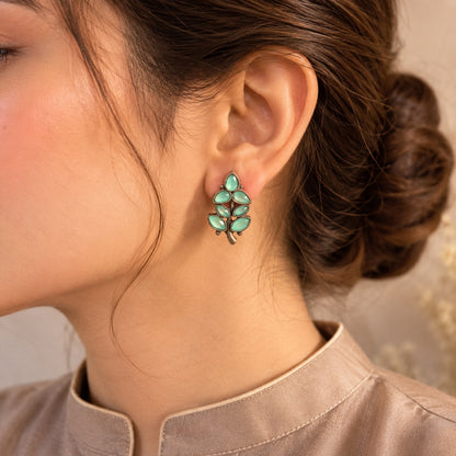 Close-up of a person wearing a green leaf-shaped earring with a neutral background