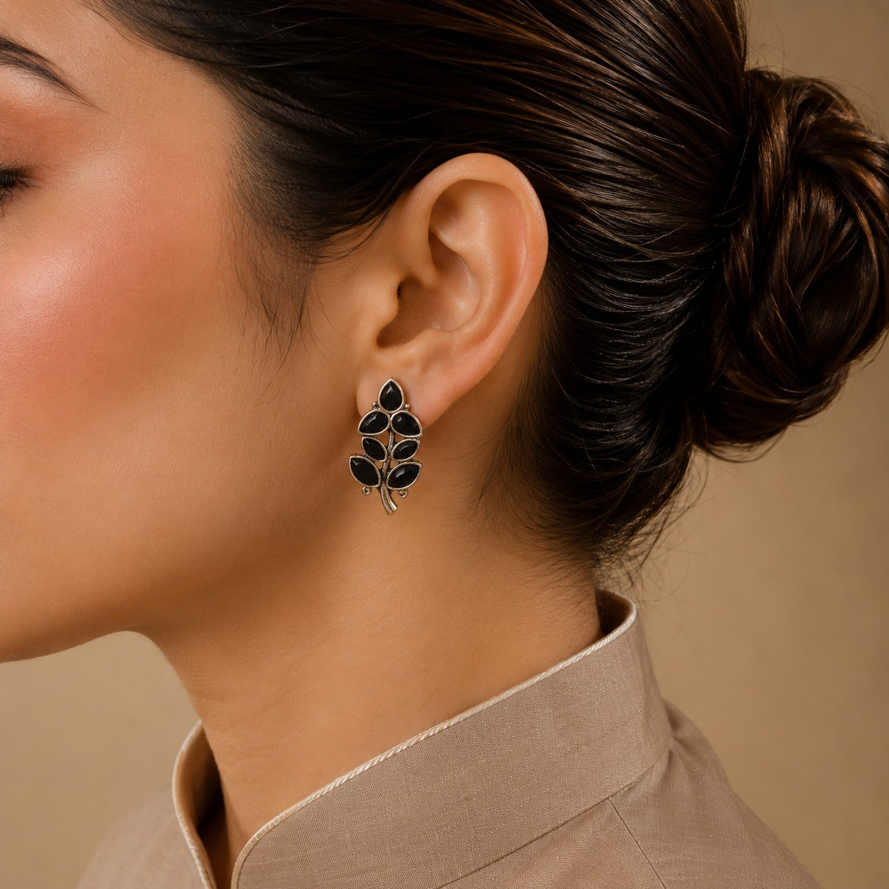Close-up of a woman wearing a leaf-shaped earring against a neutral background