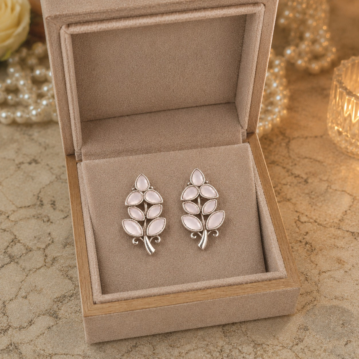 Pair of silver leaf-shaped earrings in a jewelry box on a textured surface.