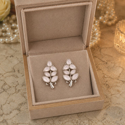 Pair of silver leaf-shaped earrings in a jewelry box on a textured surface.