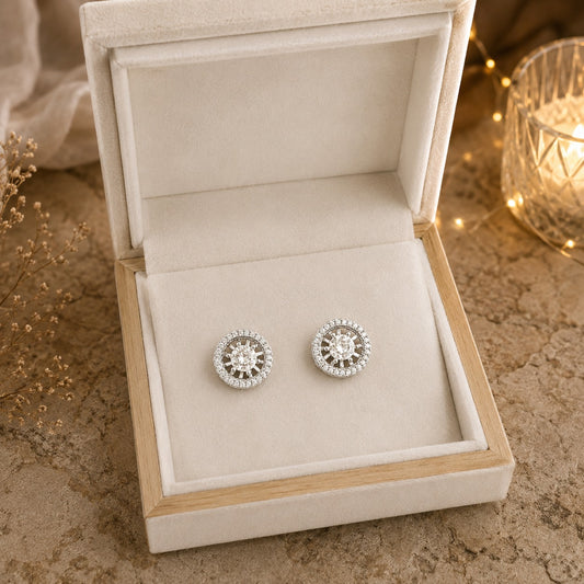 Silver earrings in a jewelry box on a textured surface with a warm glow.