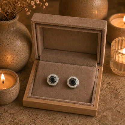 Jewelry box with a pair of earrings featuring black stones and silver accents, surrounded by candles and decorative elements.
