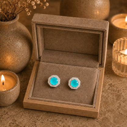 Turquoise gemstone earrings in a jewelry box with candles and decorative items in the background