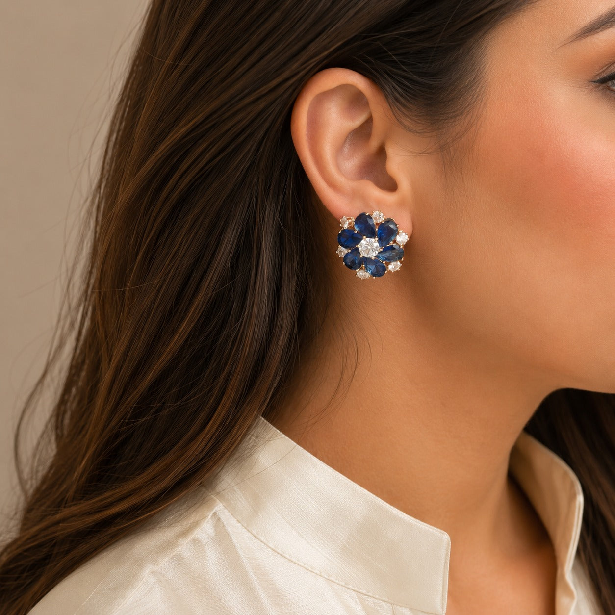 Woman wearing premium royal blue floral crystal stud earrings with pear-cut stones in a luxury side-profile portrait.