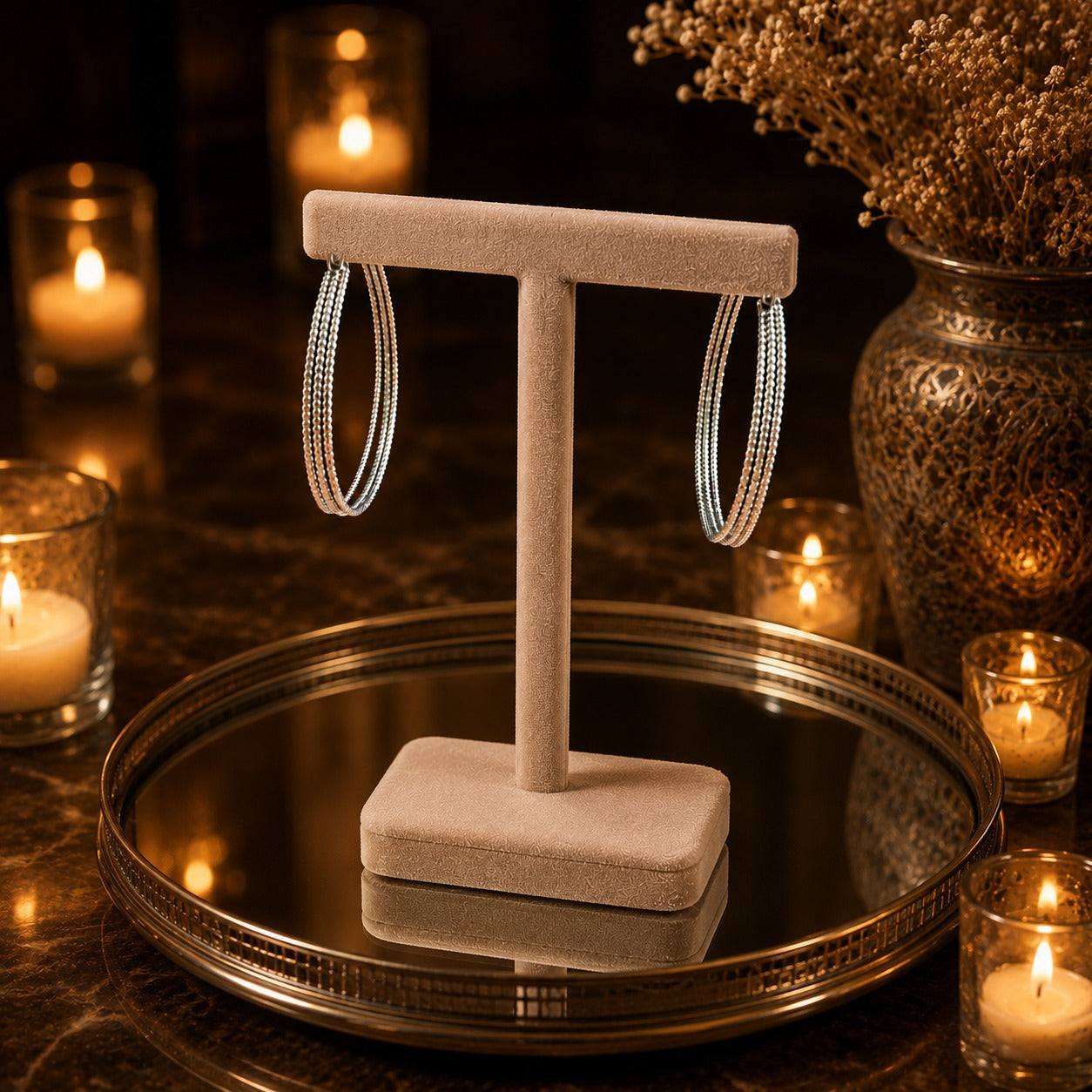 Textured silver hoop earrings showcased on a premium beige velvet jewelry stand with luxury candle-lit styling.