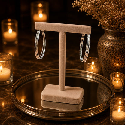Textured silver hoop earrings showcased on a premium beige velvet jewelry stand with luxury candle-lit styling.