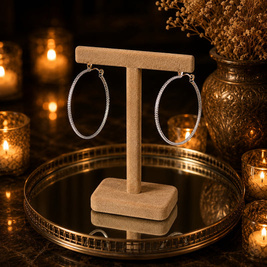 Side profile of textured silver hoop earrings displayed on a velvet jewelry stand highlighting their slim profile and textured finish.