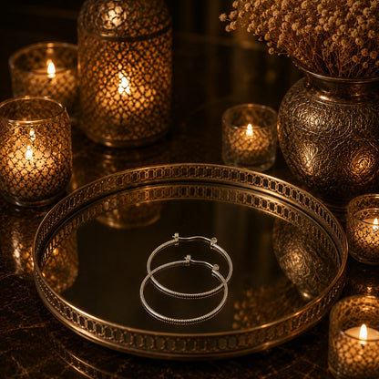 Premium textured silver hoop earrings displayed on a luxury mirrored tray with warm candlelight and decorative accents.