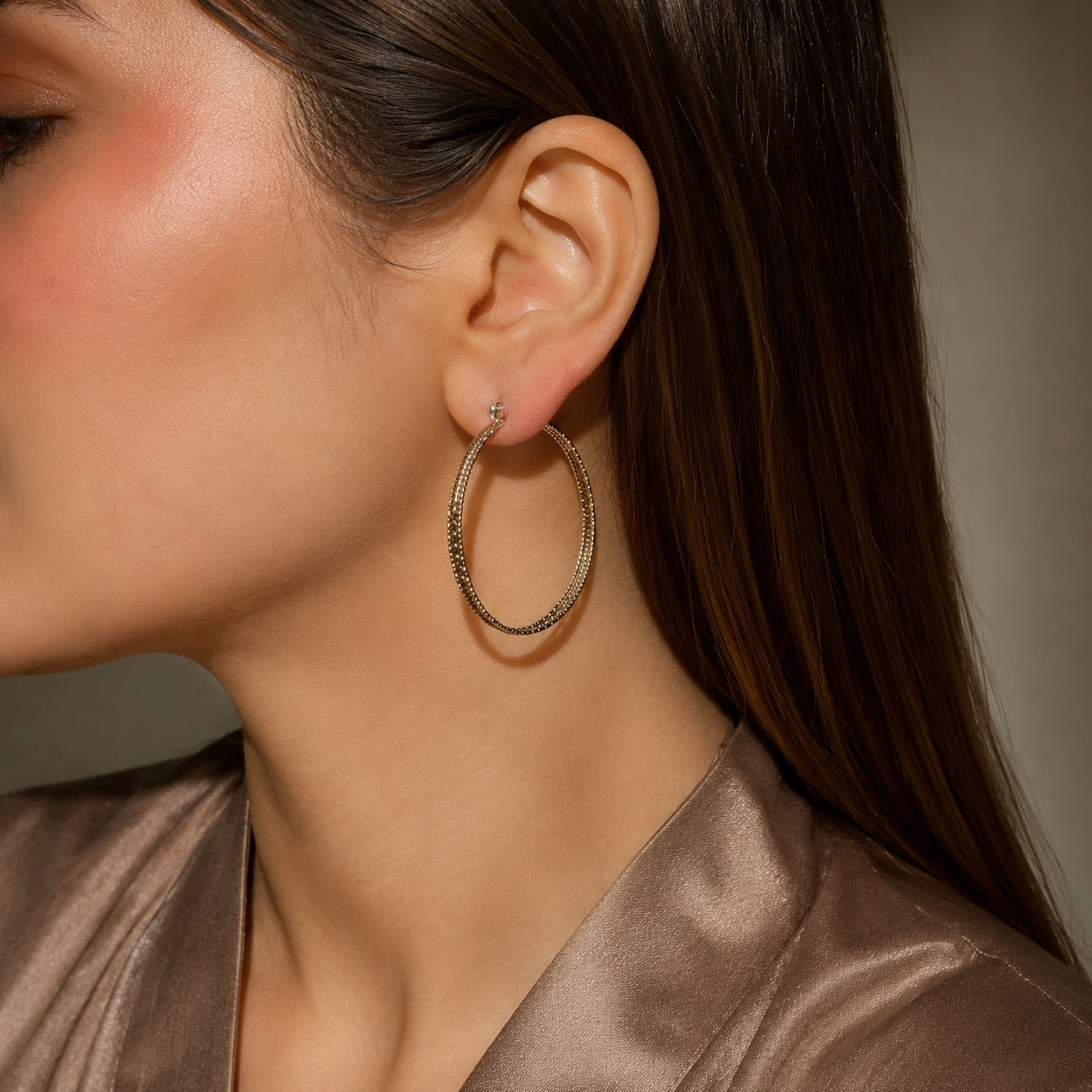 Woman wearing premium textured silver hoop earrings in a side-profile portrait with a satin taupe outfit