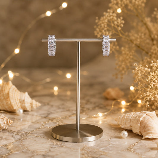 Silver baguette crystal huggie hoop earrings showcased on a luxury metal jewelry stand with soft fairy lights and elegant styling.