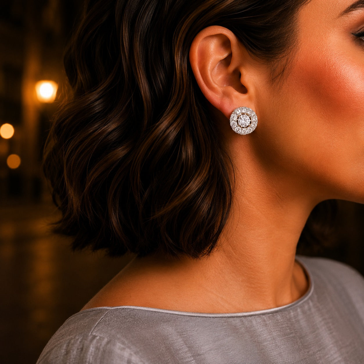 Woman wearing gold-tone crystal halo stud earrings featuring a round-cut centre stone with sparkling pavé detailing.