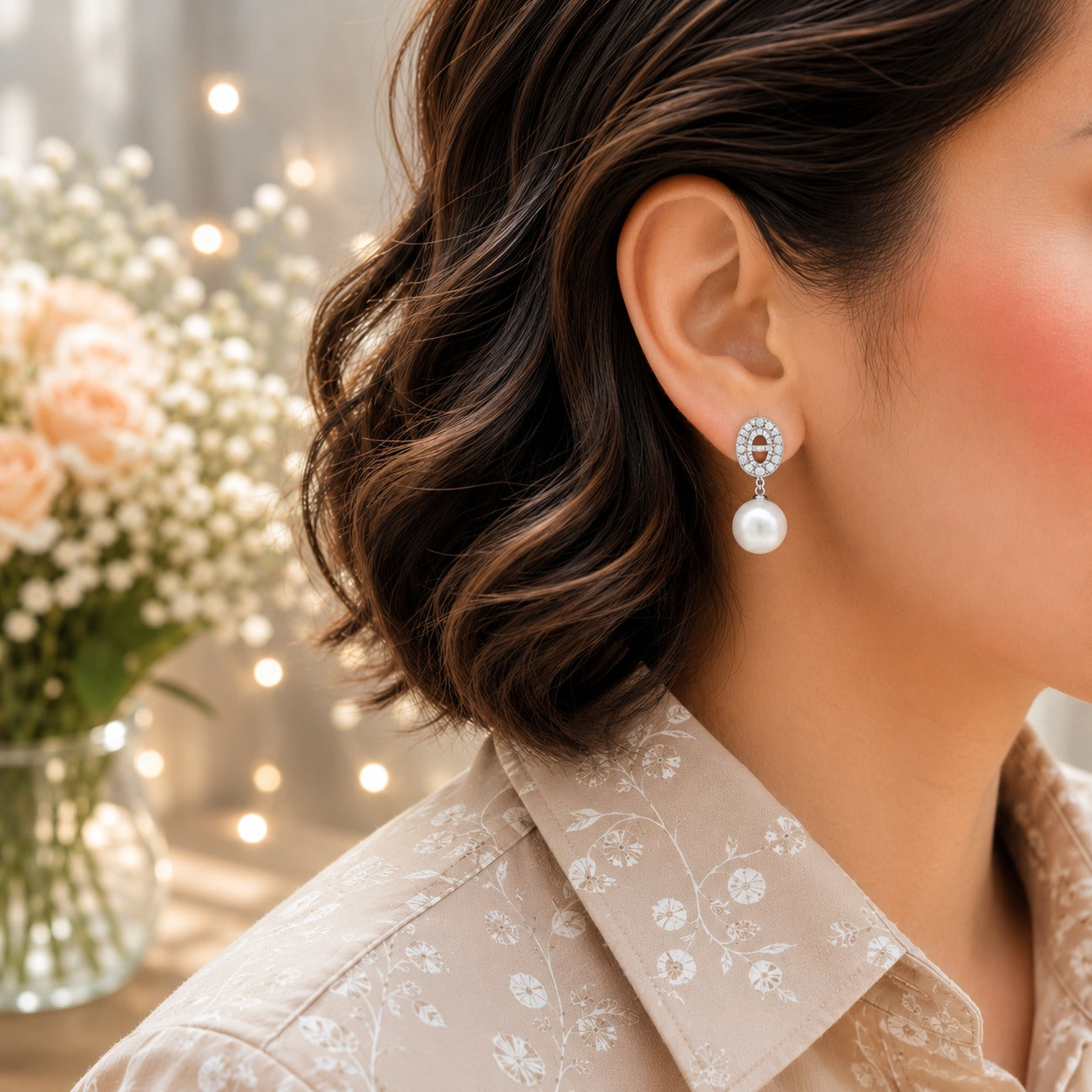Close-up of a model wearing silver oval crystal and pearl drop earrings with a sparkling pavé finish and classic pearl drop