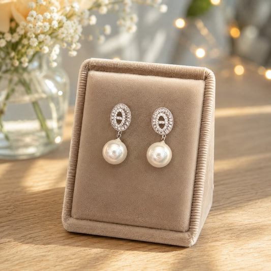 Silver crystal and pearl drop earrings displayed on a premium beige velvet jewellery stand with soft floral décor and warm fairy lights.