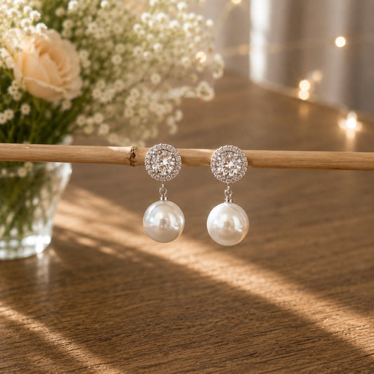 Silver halo crystal pearl drop earrings displayed on a natural bamboo display with soft floral décor and warm fairy lights.