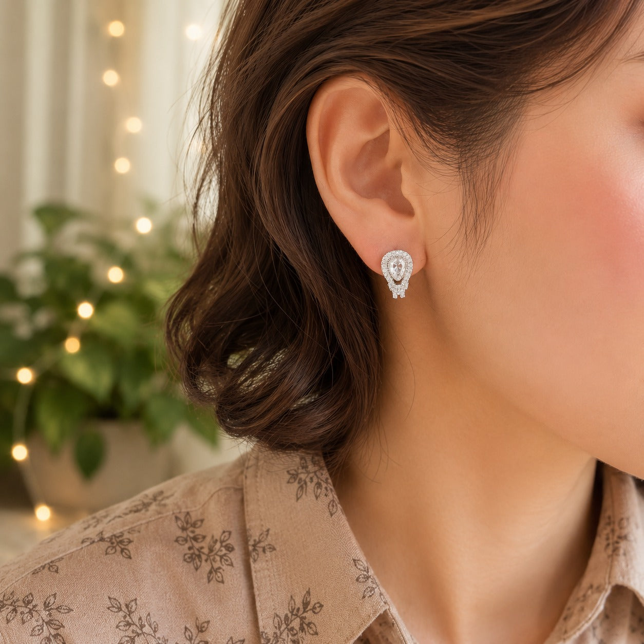 Woman wearing pear halo drop crystal stud earrings with a taupe printed linen shirt in a close-up portrait.