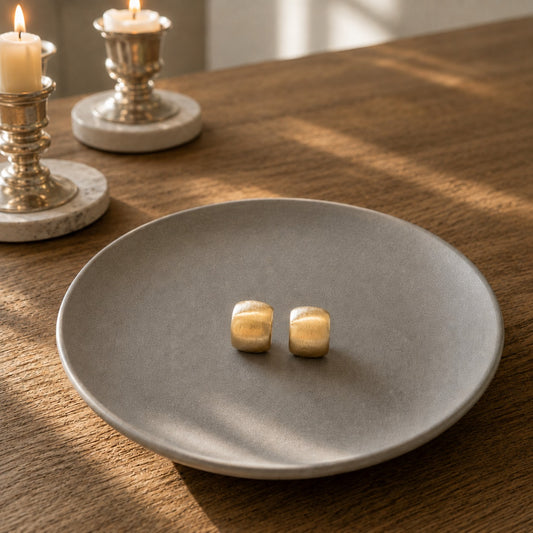 Pair of matte gold mini huggie hoop earrings displayed on a grey ceramic plate with brushed matte finish.