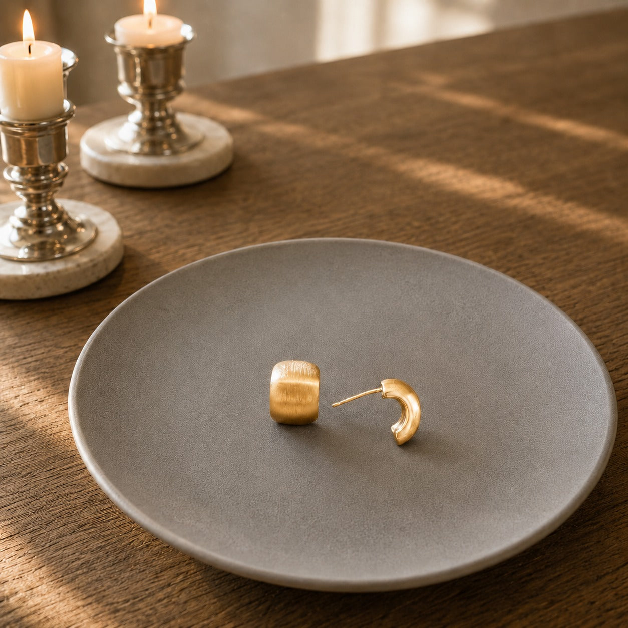 Side view of Pair of matte gold mini huggie hoop earrings displayed on a grey ceramic plate with brushed matte