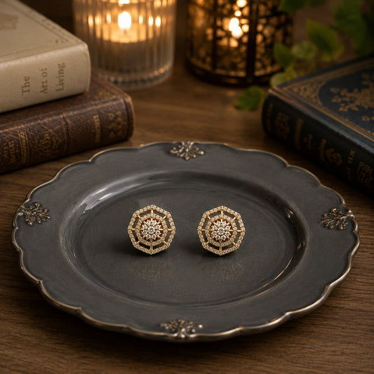 Geometric halo crystal stud earrings displayed on a premium charcoal grey ceramic plate with vintage books, candlelight, and lantern décor.