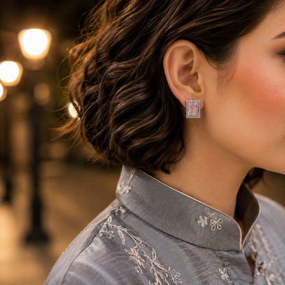 Woman wearing radiant emerald-cut crystal stud earrings with a soft grey embroidered linen shirt in a close-up portrait.