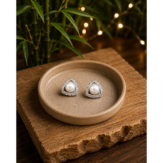 Pearl triangle crystal stud earrings displayed on a premium beige ceramic dish placed on a rustic wooden slab with bamboo, fairy lights, and a softly blurred background.