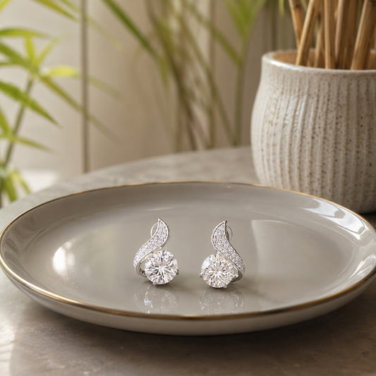 Silver twist solitaire crystal stud earrings displayed on a grey ceramic plate with soft natural décor and a modern indoor setting.